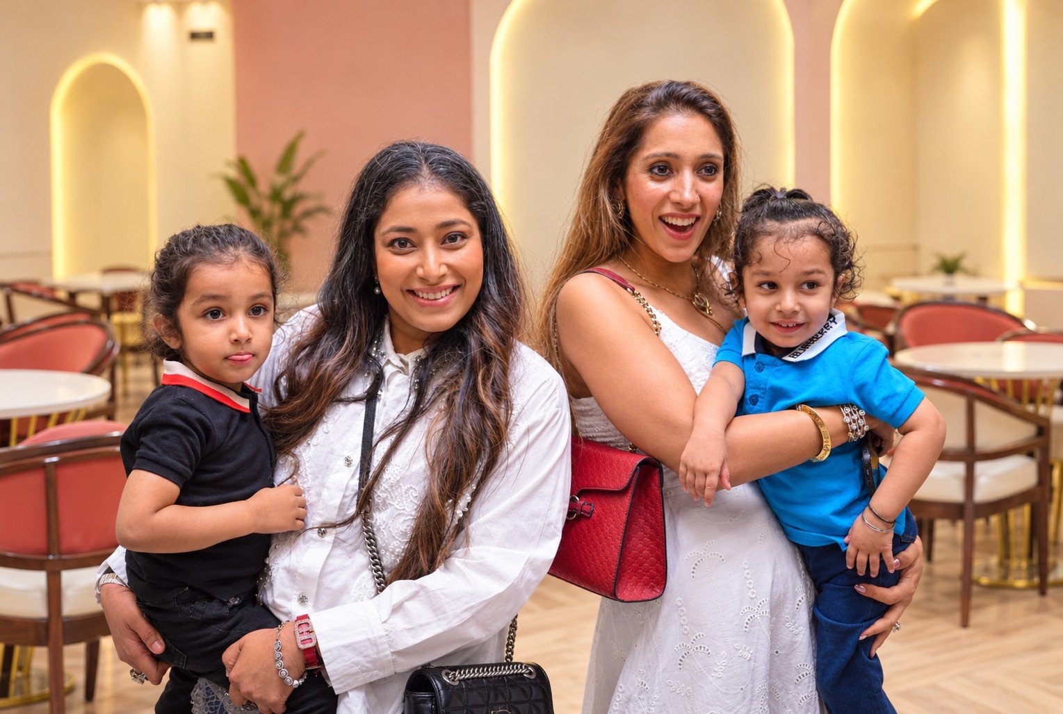 Two smiling mothers holding their young children in the arched party hall at OWI Kids World