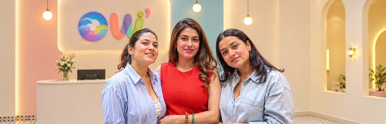 Three smiling mothers posing at the OWI Kids World reception desk in Chattarpur, South Delhi